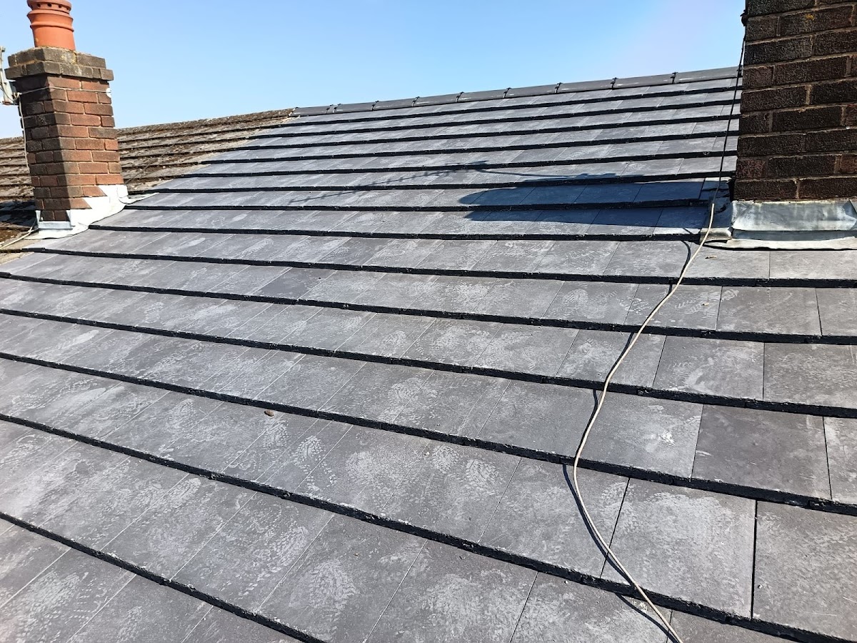 Pitched roof with overlapping grey roof tiles, brick chimneys and metal flashing